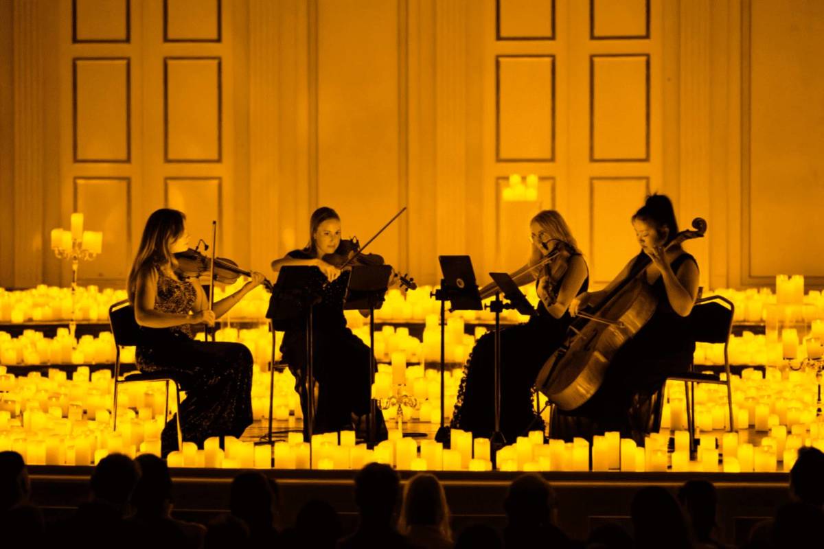 four women play a string quartet with candles surrounding them