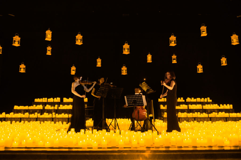 Cuarteto de cuerdas sobre un escenario lleno de velas de Candlelight y farolillos en el techo