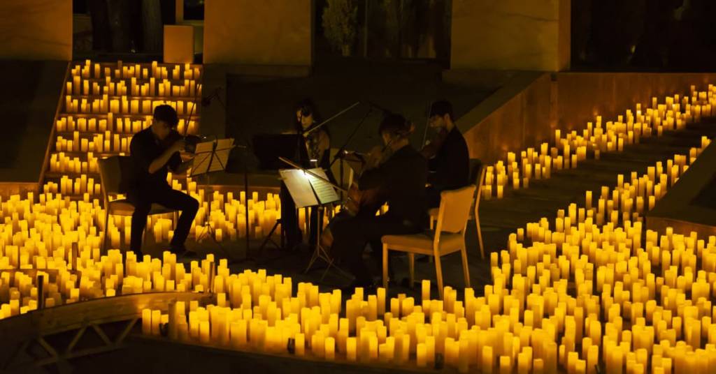 Un cuarteto de cuerda toca sobre un escenario cubierto de velas durante un concierto Candlelight.