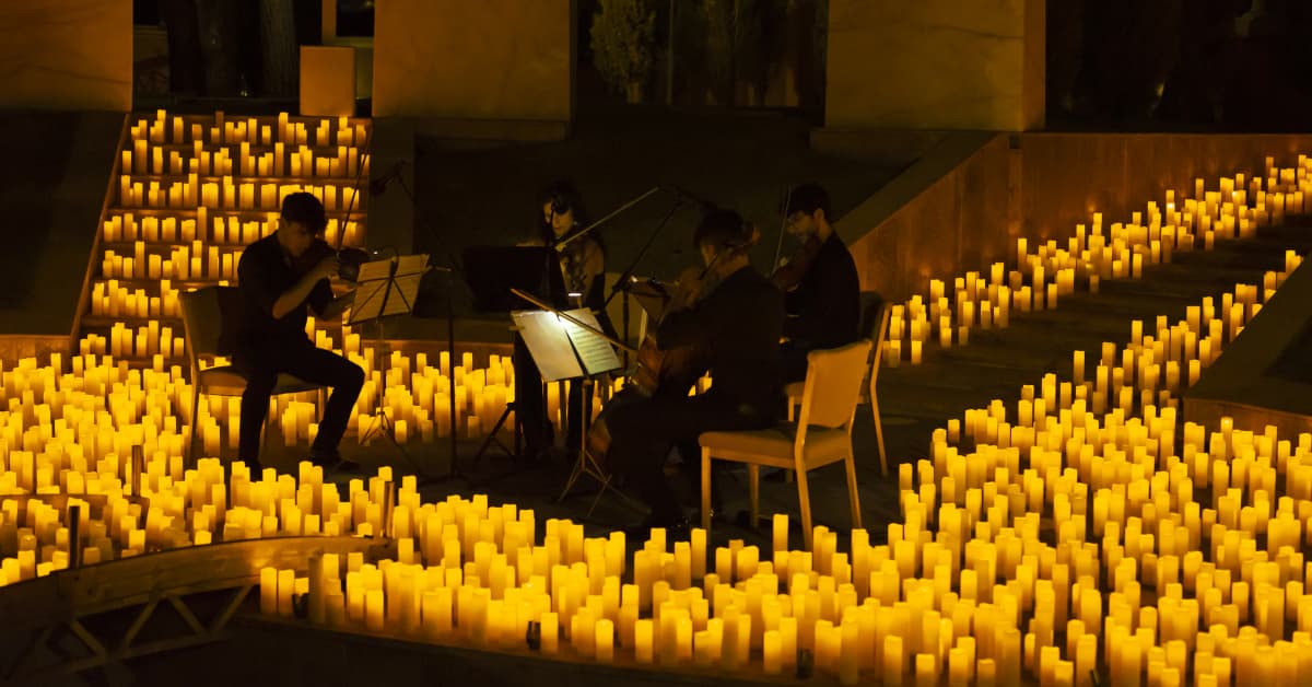 Un cuarteto de cuerda toca sobre un escenario cubierto de velas durante un concierto Candlelight.