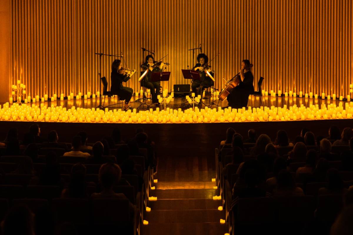 A string quartet sits on stage surrounded by thousands of candles
