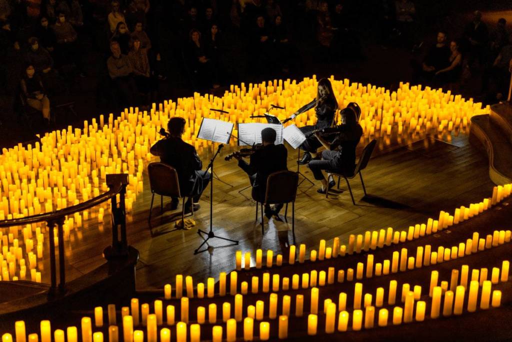 Un cuarteto de cuerda toca sobre un escenario cubierto de velas durante un concierto Candlelight.