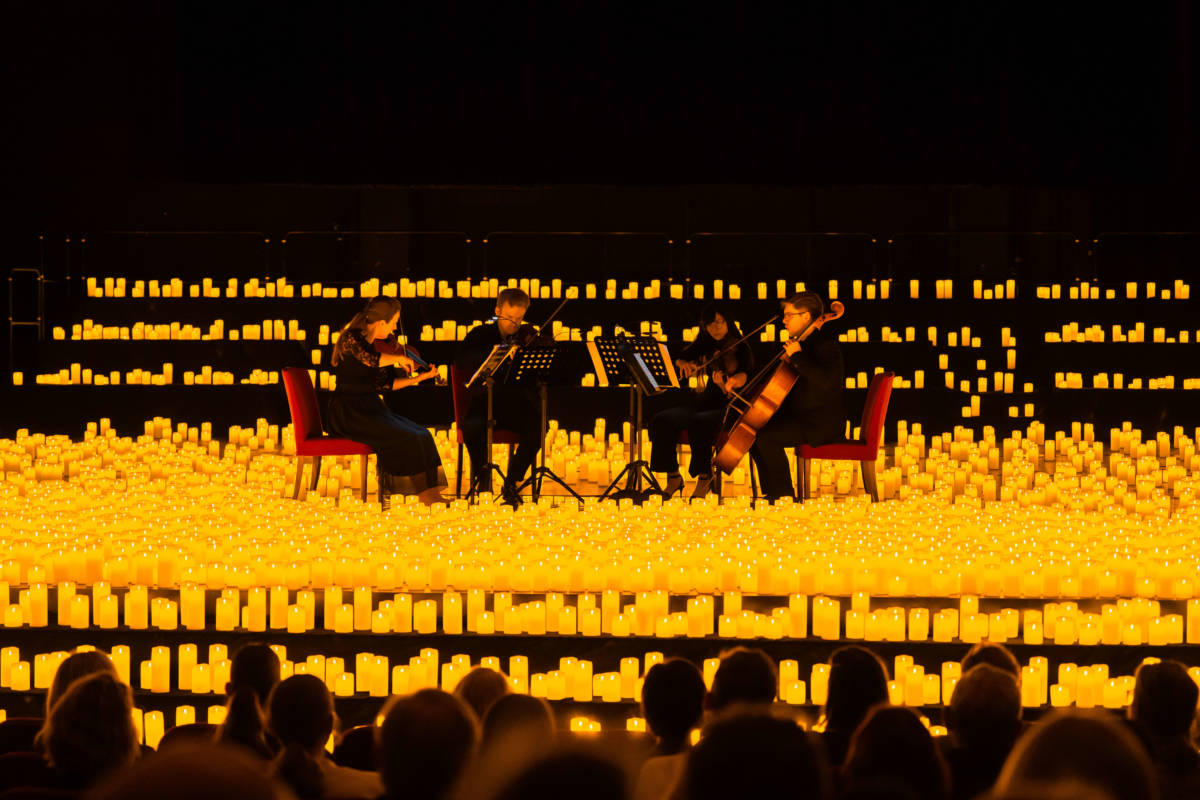 Un cuarteto de cuerda toca sobre un escenario cubierto de velas durante un concierto Candlelight.