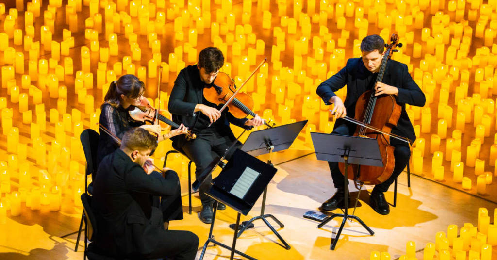 A string quartet performing live at a Candlelight concert on a stage illuminated by thousands of candles.