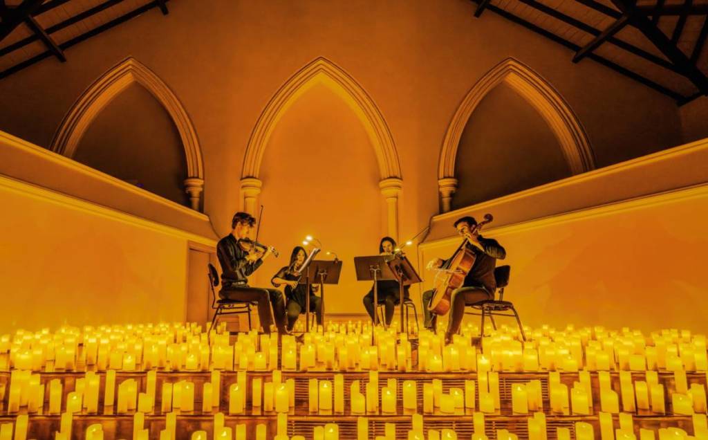 Un cuarteto de cuerda toca sobre un gran escenario cubierto de cálidas velas durante un concierto Candlelight.