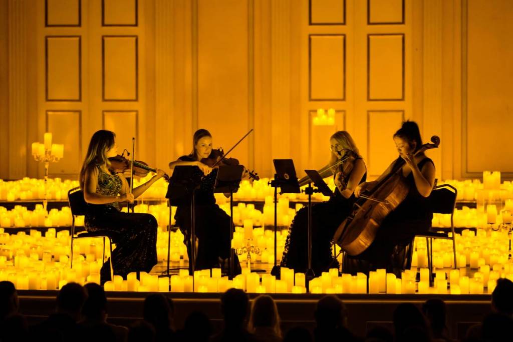 Ein Streichquartett spielt bei einem Candlelight-Konzert auf einer mit Kerzen bedeckten Bühne.