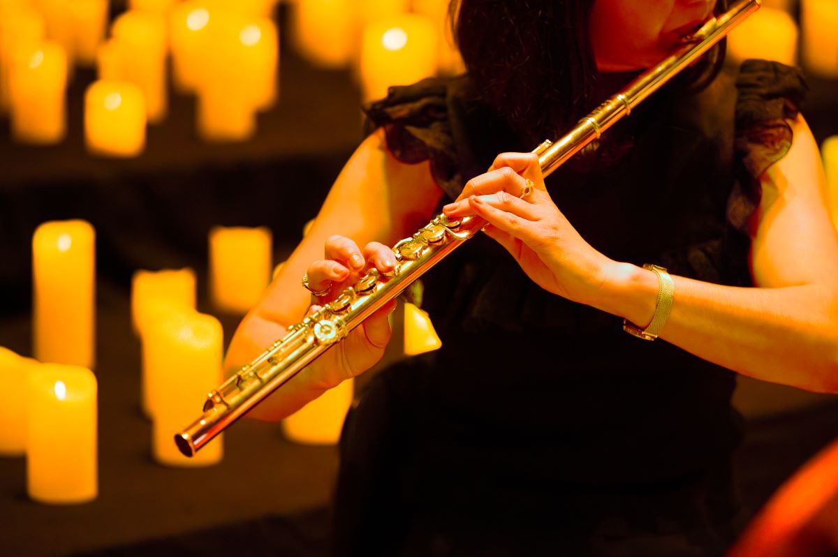 Frau spielt bei einem Candlelight Konzert auf einer Querflöte, Kerzen im Hintergrund