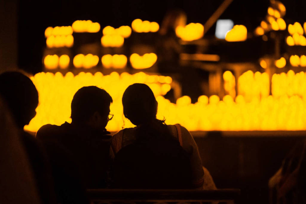Dos espectadores miran atentos hacia el escenario cubierto de velas donde un músico toca el piano durante un concierto Candlelight.