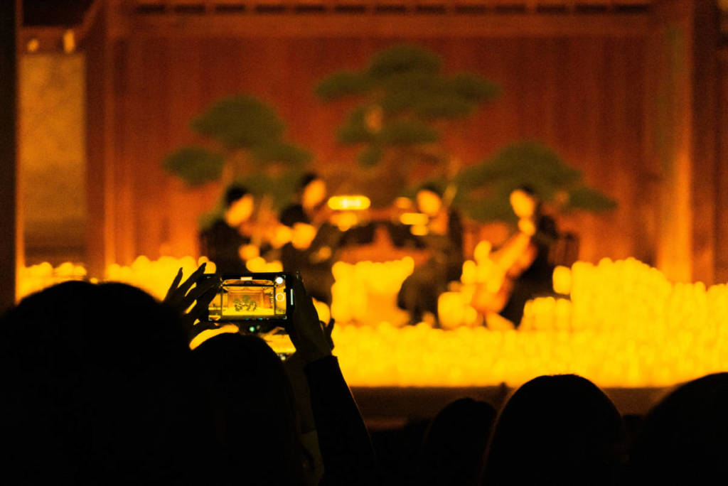Un espectador graba con el móvil a un cuarteto sobre un escenario cubierto de velas durante un concierto Candlelight.