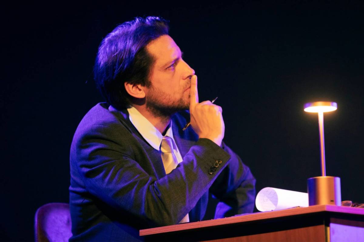 Der Verteidiger sitzt bei The Jury Experience an seinem Tisch und hält seinen Finger in einer nachdenklichen Pose an seinen Mund.