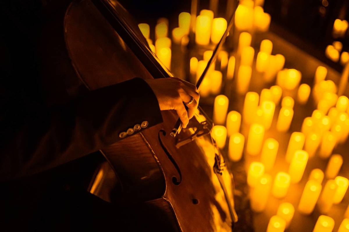 Primer plano de la mano de una violonchelista sobre un escenario cubierto de velas durante un concierto Candlelight.