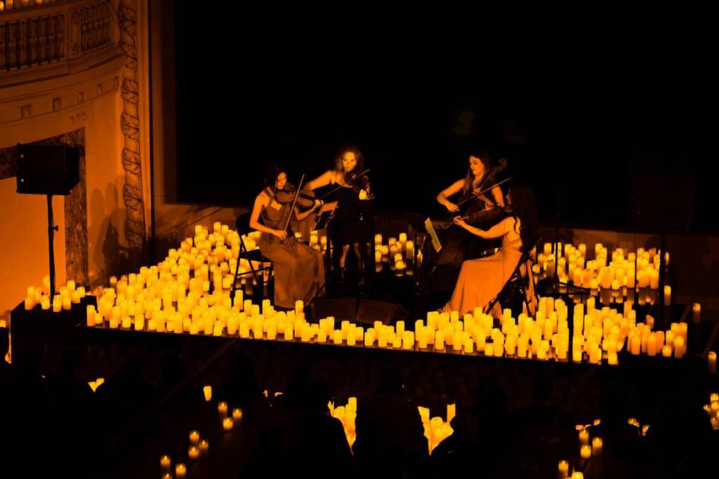 women play string instruments forming part of string quartet on stage surrounded by candles