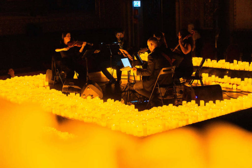 Un cuarteto de cuerda toca sobre un escenario cubierto de velas durante un concierto Candlelight.