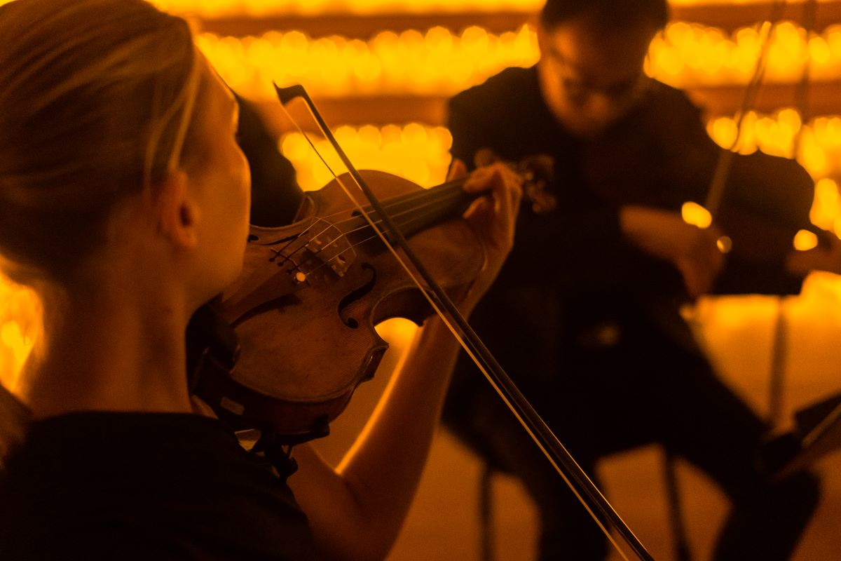 Frau spielt bei einem Candlelight-Konzert auf einer Violine, mit Kerzen und anderen Musikern im Hintergrund