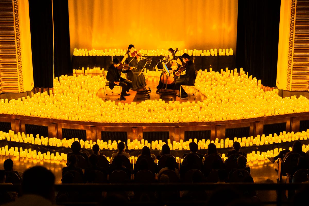 Streichquartett spielt bei einem Candlelight-Konzert auf der Bühne, umringt von etlichen Kerzen. Publikum im Vordergrund.