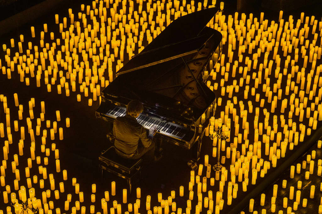 Photo d'un piano et son pianiste vu en plongée entouré de milliers de bougies lors d'un concert Candlelight