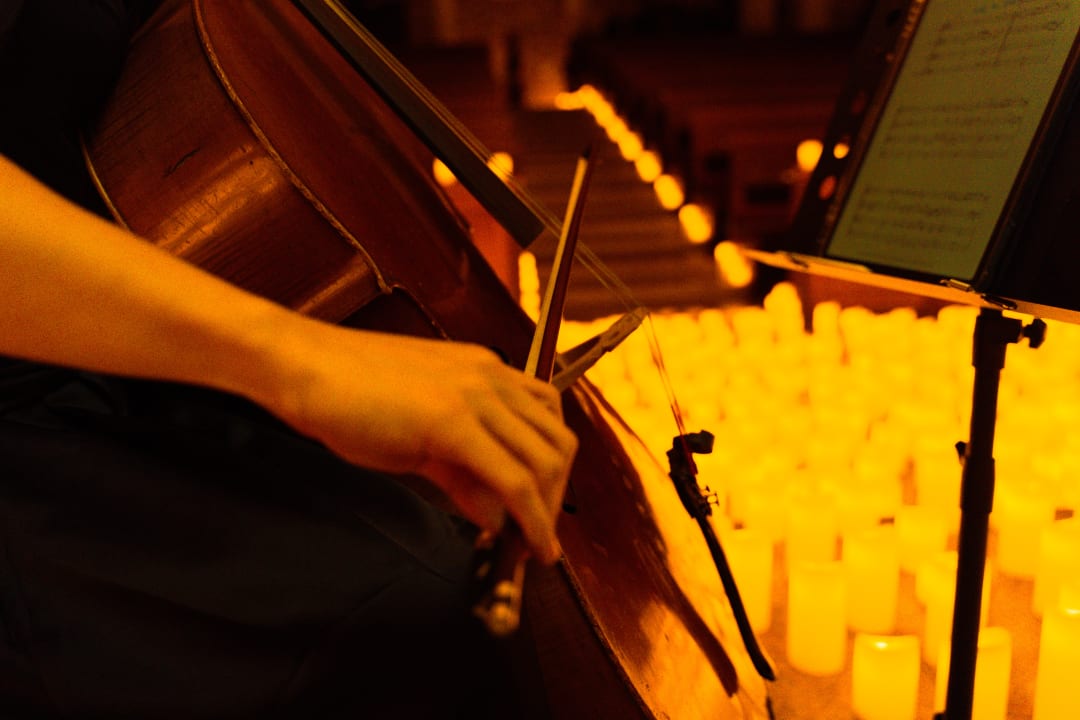 Un gros plan sur un violoncelle avec des milliers de bougies en fond