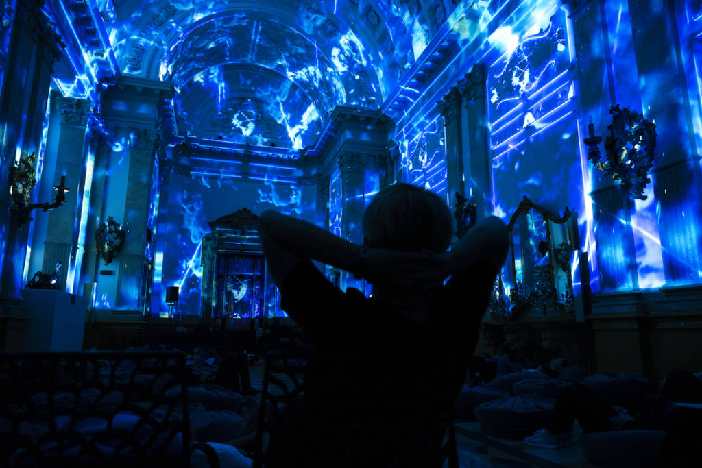 a silhouette of a person leaning back as they admire the stormy projections of the Enlightenment show