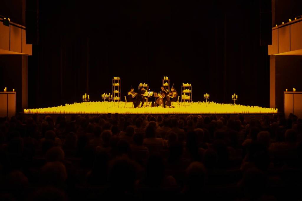 A wide shot of a string quartet performing inside a theatre, surrounded by thousands of candles at a Candlelight concert