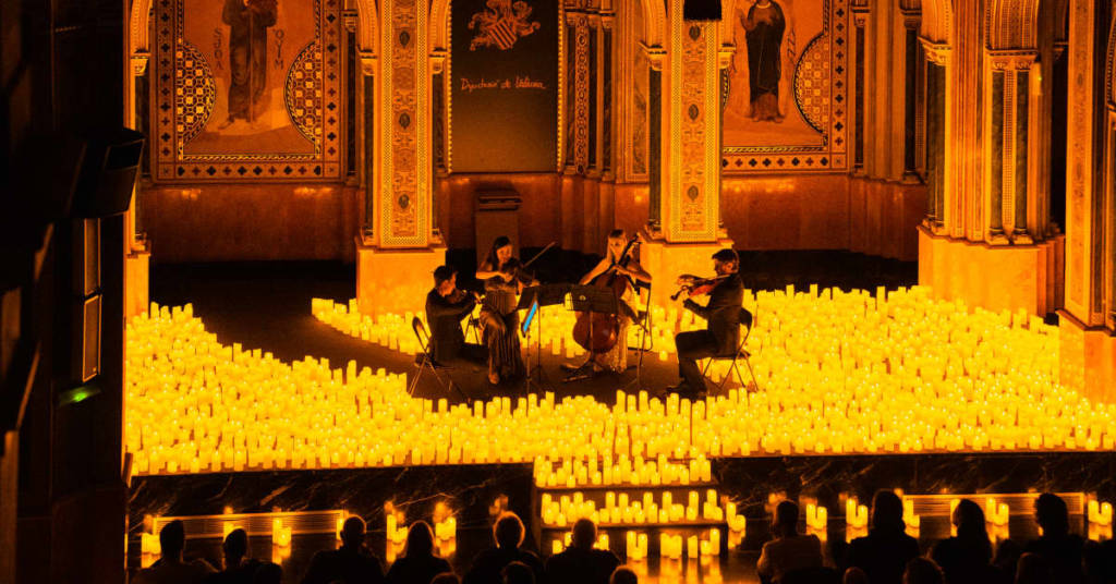 Un cuarteto de cuerda toca sobre un escenario cubierto de velas durante un concierto Candlelight.