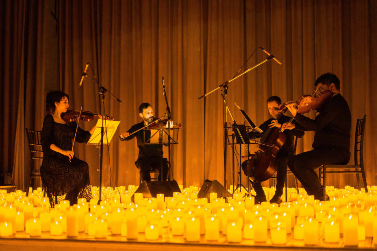 Un cuarteto de cuerda toca sobre un escenario cubierto de velas durante un concierto Candlelight.
