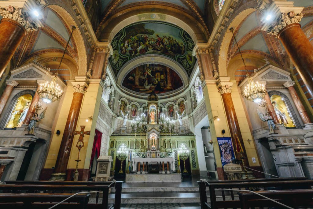 Interior de la Basílica del Sagrado Corazón de Jesús de La Plata, con su altar mayor, columnas decoradas y cúpula con frescos religiosos iluminados por lámparas