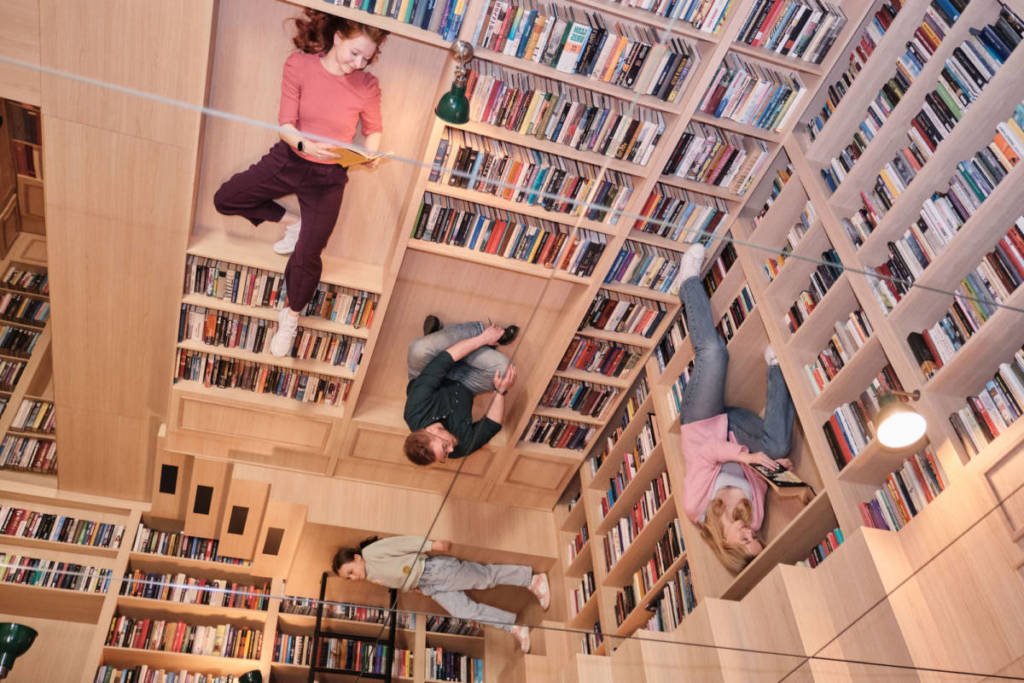 a group of people appear to lie on the ceiling in bookshelves at the Paradox Museum