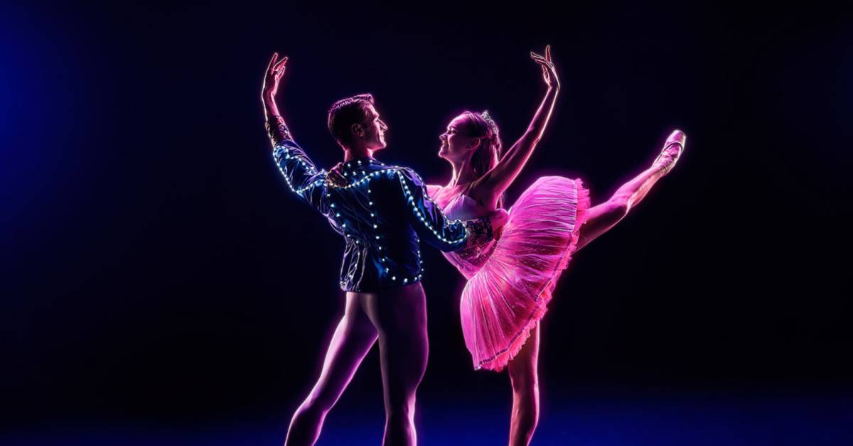casal de bailarinos com figurinos iluminados em palco escuro
