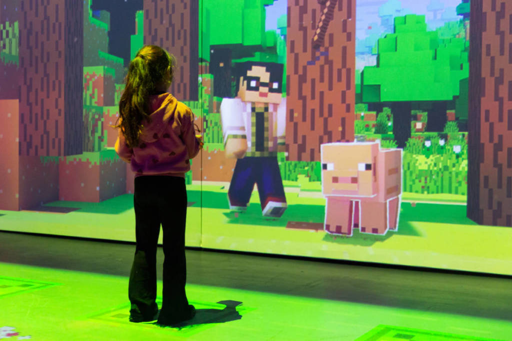 a girl interacts with a digital wall displaying a Minecraft scene at Minecraft Experience: Villager Rescue