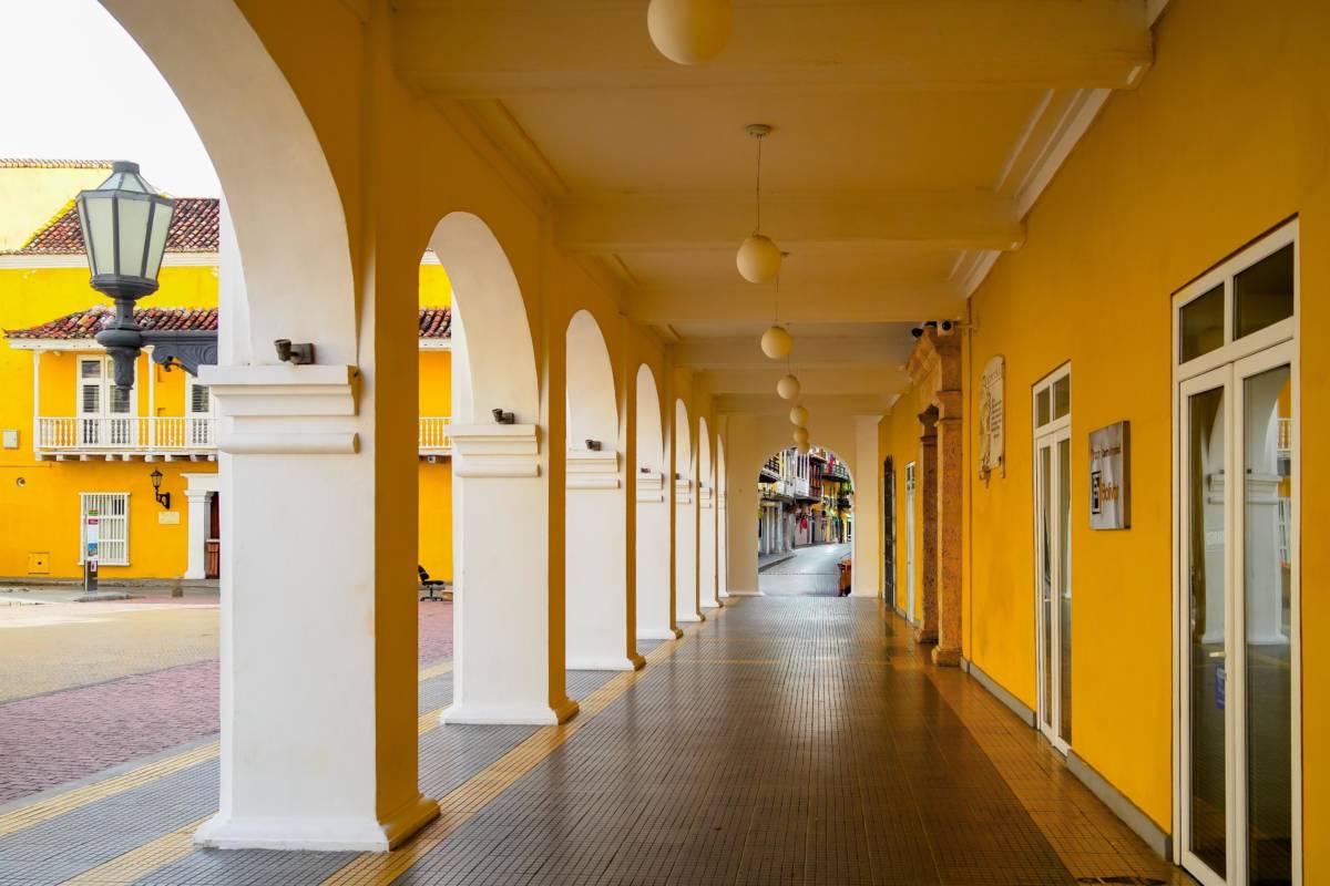 Pasillo porticado del Palacio de la Proclamación en Cartagena, con arcos blancos alineados, muros amarillos y vista a la calle colonial al fondo