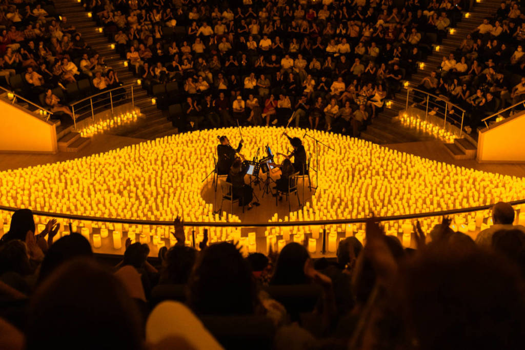 Concierto Candlelight de cuarteto de cuerda en un escenario lleno de velas y rodeado de público en sus butacas