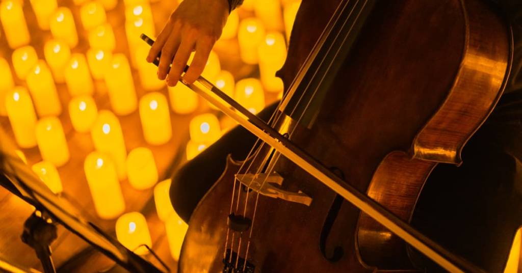Primer plano de un músico tocando el violonchelo durante un concierto Candlelight iluminado por miles de velas.