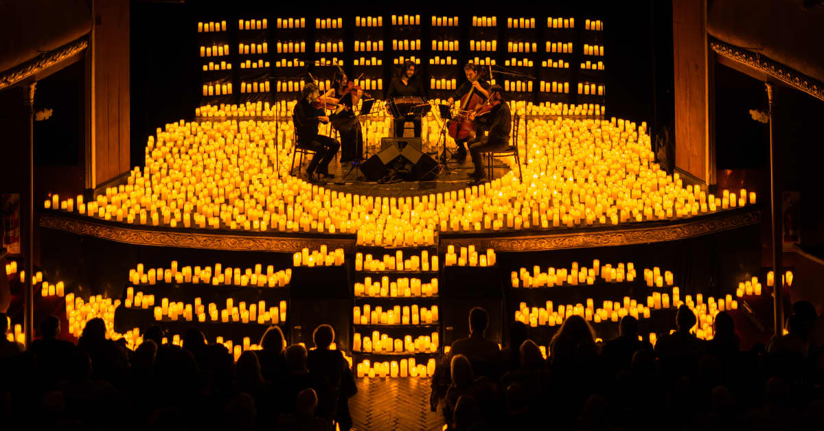 Plano general de un cuarteto de cuerda tocando sobre un escenario cubierto de miles de velas durante un concierto Candlelight.