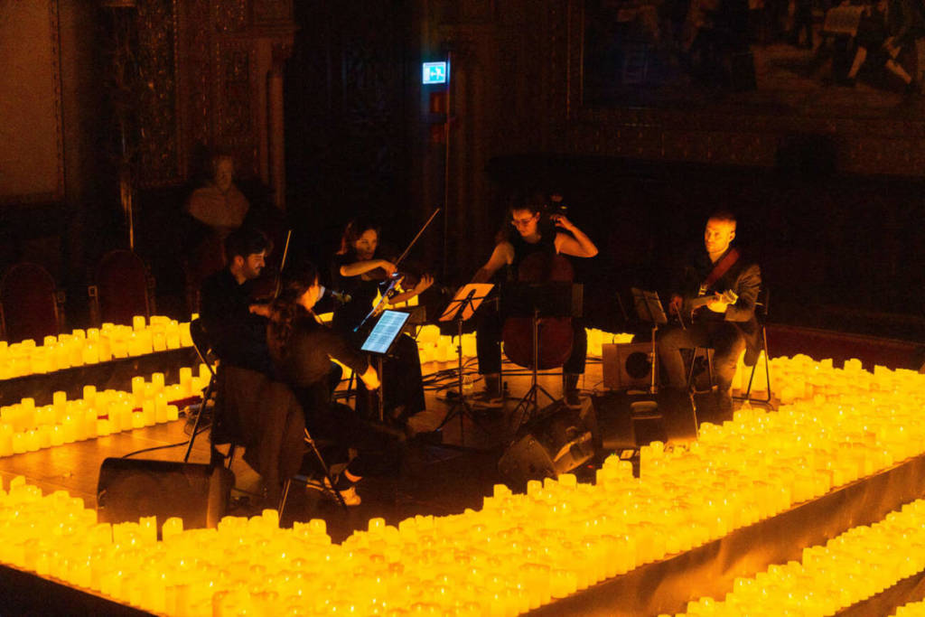 Un cuarteto de cuerda toca sobre un escenario cubierto de velas durante un concierto Candlelight.