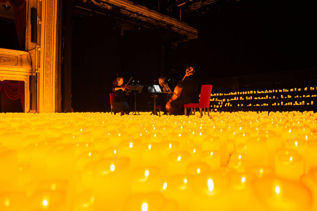 Un cuarteto de cuerda toca sobre un escenario cubierto de velas durante un concierto Candlelight.