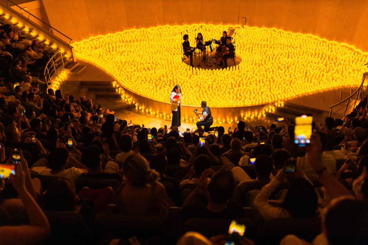 Un hombre le pide matrimonio a su novia delante de un escenario cubierto de velas sobre el que hay un cuarteto de cuerda durante un concierto Candlelight.