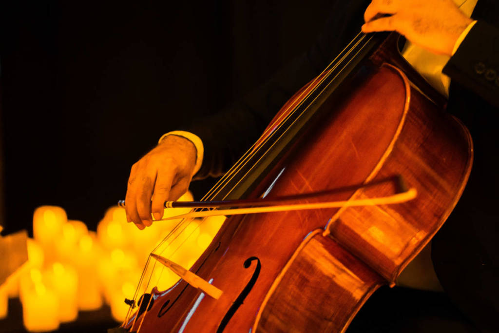 Primer plano de un músico tocando el violonchelo sobre un escenario cubierto de velas durante un concierto Candlelight.