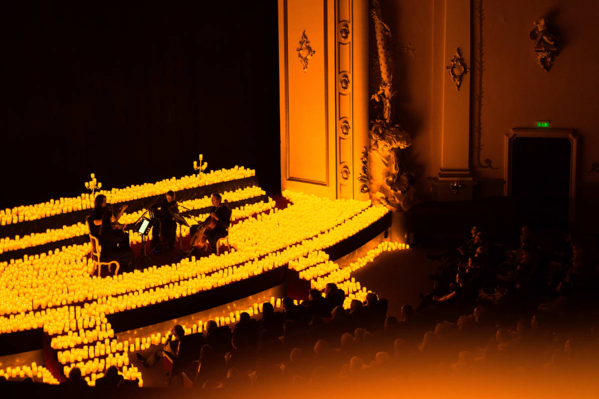 Plano general de un cuarteto de cuerda tocando sobre un escenario cubierto de velas durante un concierto Candlelight.