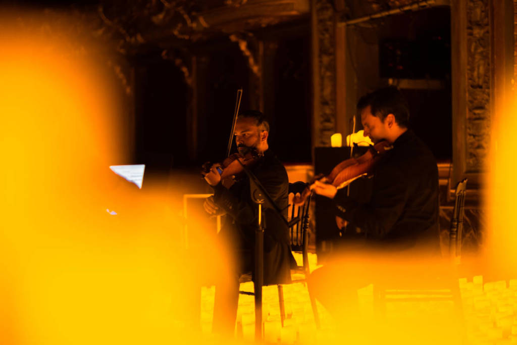 Doi violoniști cântă pe o scenă acoperită cu lumânări calde în timpul unui concert Candlelight.