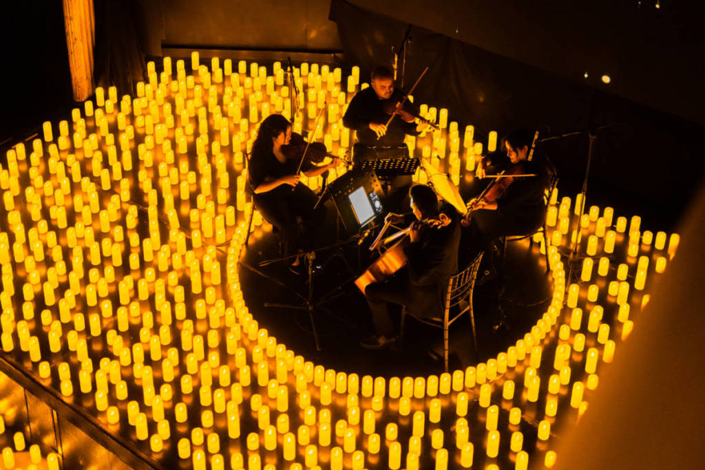 Un quartetto d’archi si esibisce su un palco ricoperto da migliaia di candele durante un concerto Candlelight
