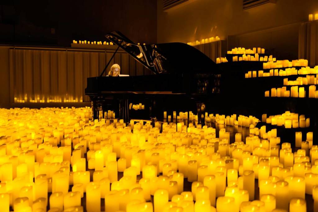 Hav av levande ljus omger en pianist och hennes piano under hennes framträdande på scen.