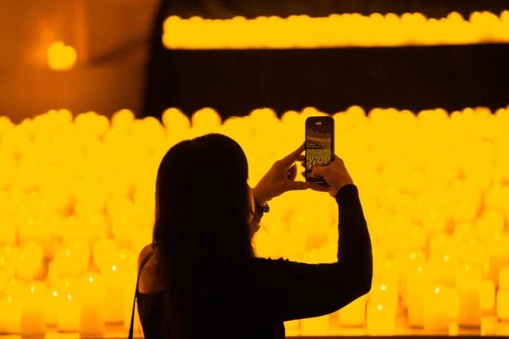 Una chica hace fotos a un escenario cubierto de miles de velas en un concierto Candlelight.