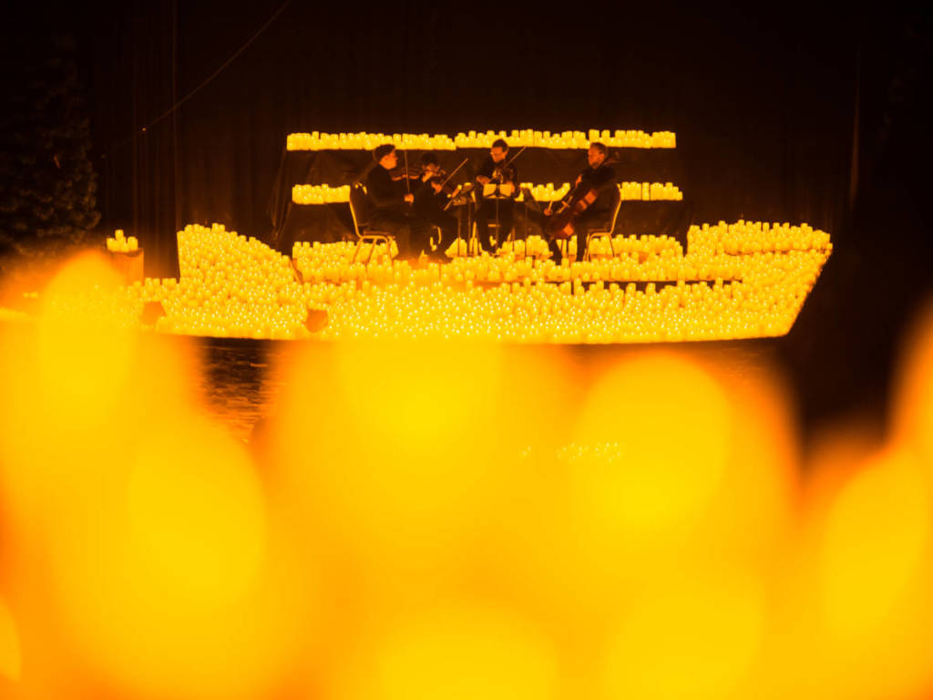 Un cuarteto de cuerda toca sobre un escenario cubierto de miles de velas durante un concierto Candlelight.
