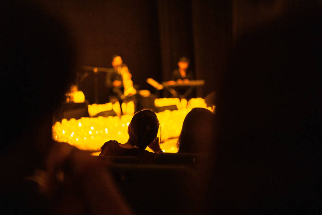 Silueta de un espectador que mira atento hacia un escenairo cubierto de miles de velas durante un concierto Candlelight.