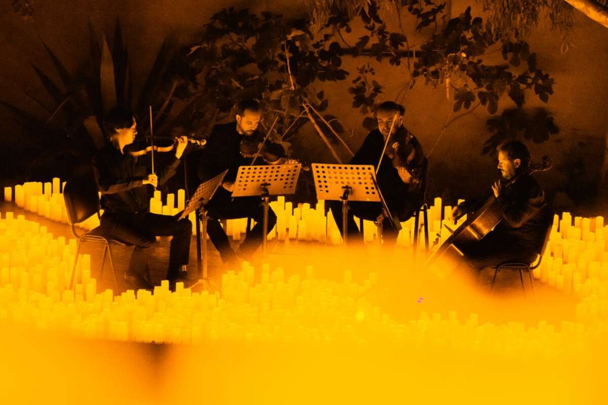 Un cuarteto de cuerda toca sobre un escenario cubierto de velas durante un concierto Candlelight.