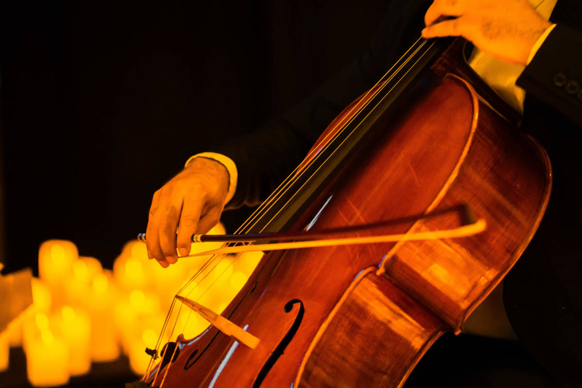Pimer plano de las manos de un músico tocando el violonchelo sobre un escenario cubierto de velas durante un concierto Candlelight.