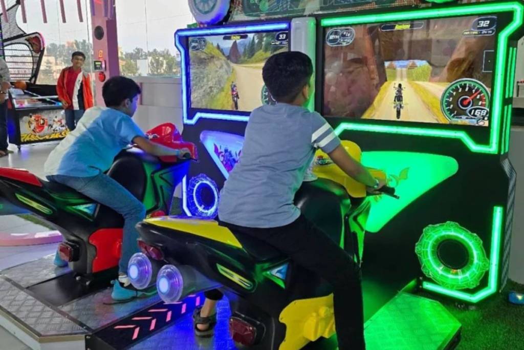 Two children playing a motorbike-themed arcade game at KAGS Fun Zone