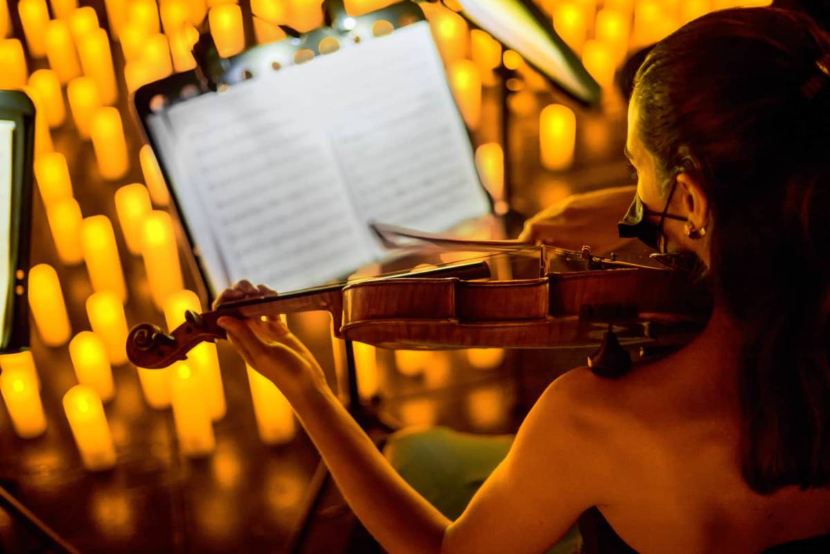 Photo d'une violoniste et de sa partition autour d'une mer de bougies pour un concert Candlelight