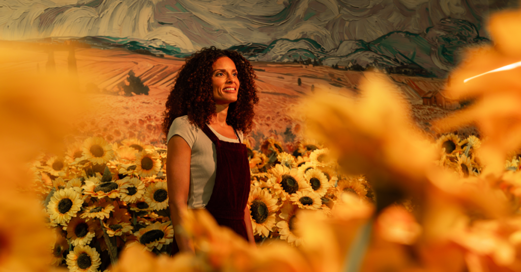 A woman walking through sunflowers as Van Gogh's paintings are projected on the walls