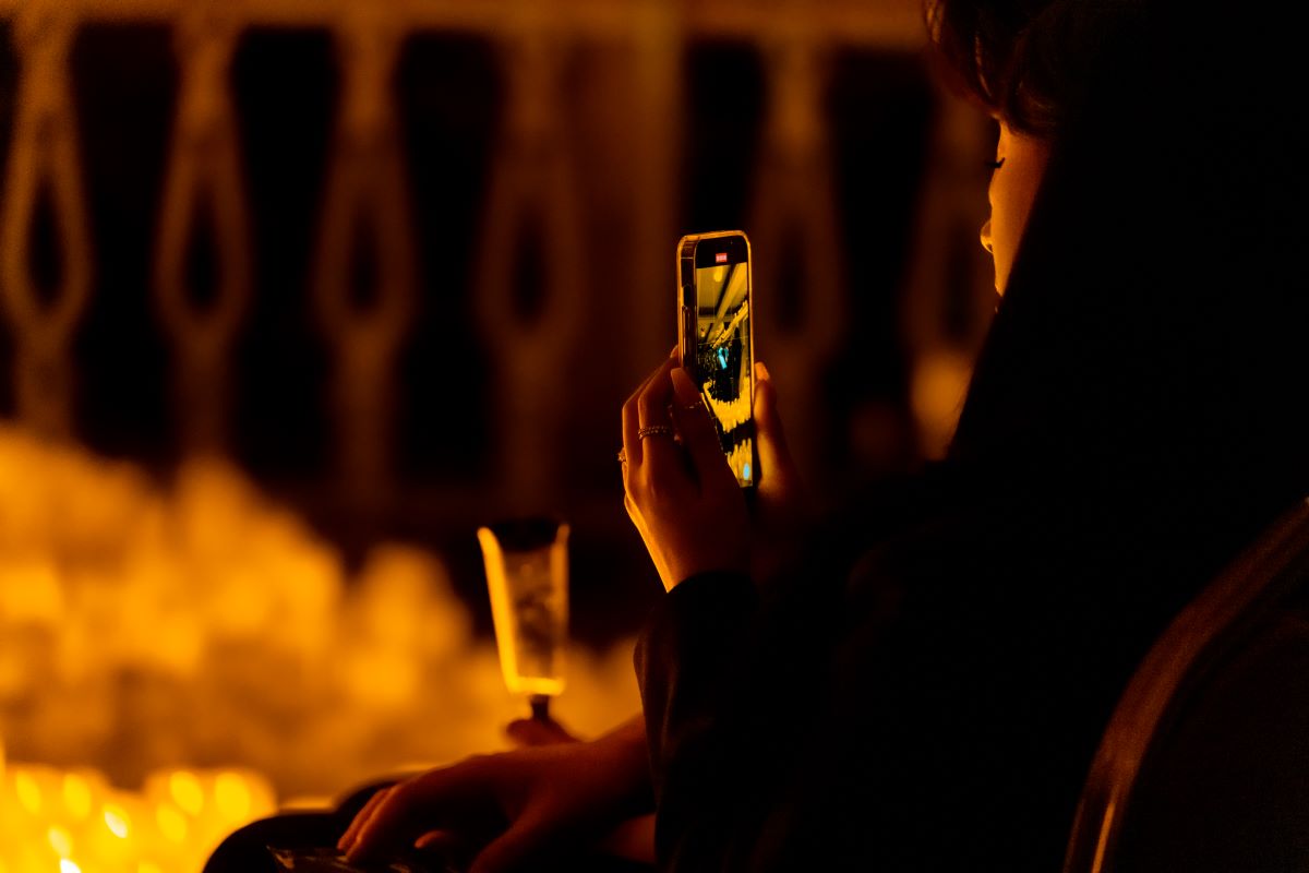 An audience member holding a glass of bubbles and her phone at a Candlelight concert.